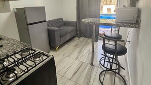 A compact kitchen with a gas stove, a refrigerator, a sofa, and a small dining area with a bar stool. - Charming studio in the Heart of Sosua, Facing the pool & at 2 min from the Beach (Sosúa)