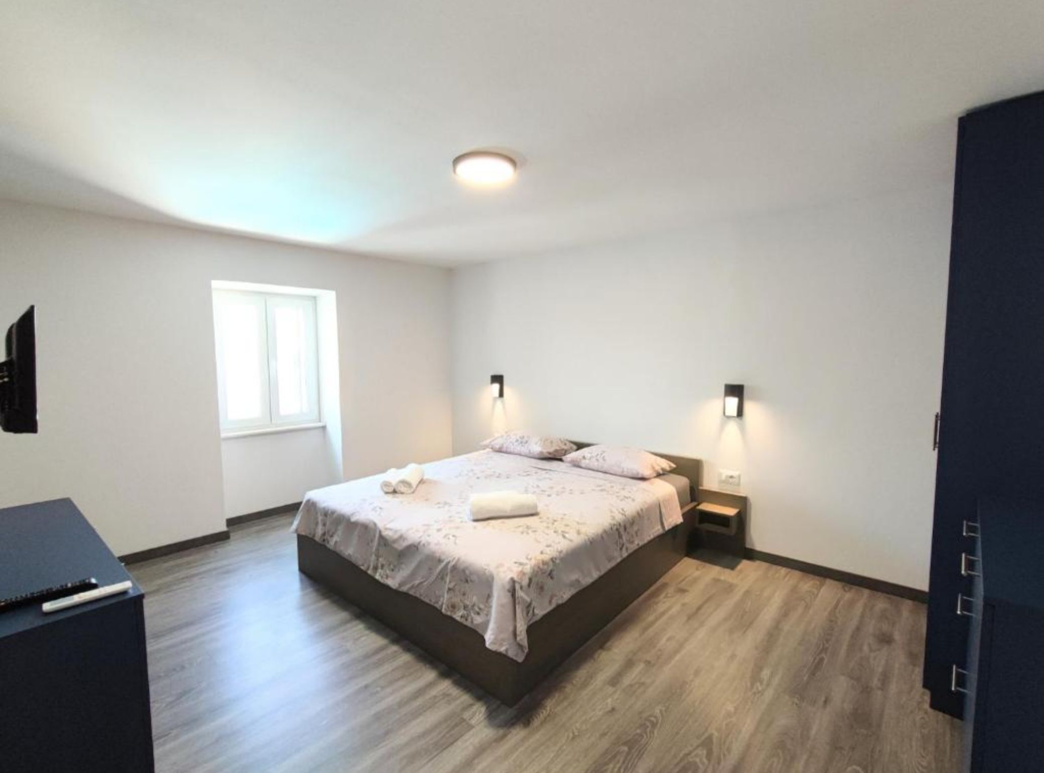 Ein modernes Schlafzimmer mit einem Bett, Nachttischen, einem Flachbildfernseher und einem Fenster.