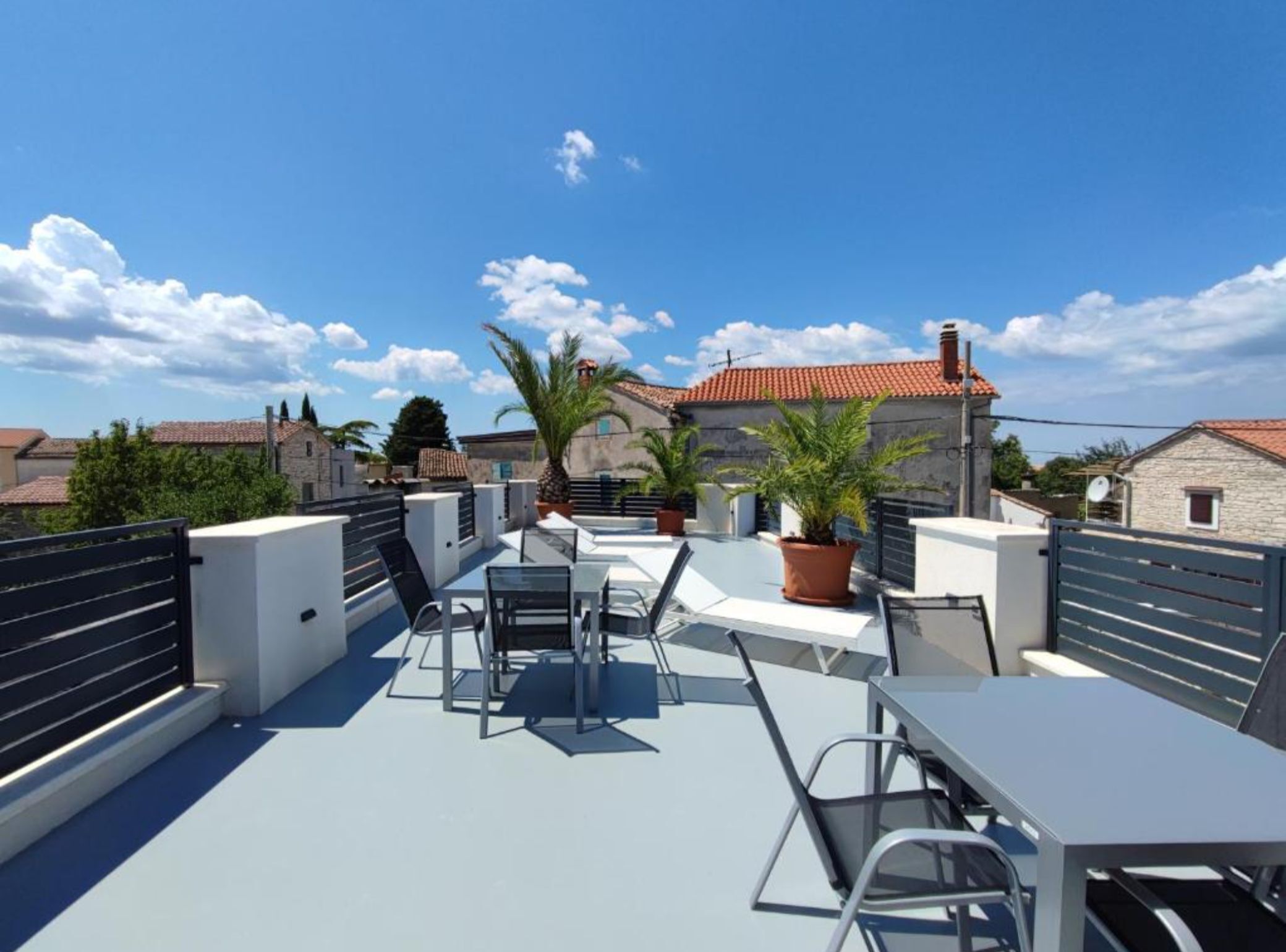 A rooftop terrace with outdoor seating, potted plants, and a view of surrounding buildings.