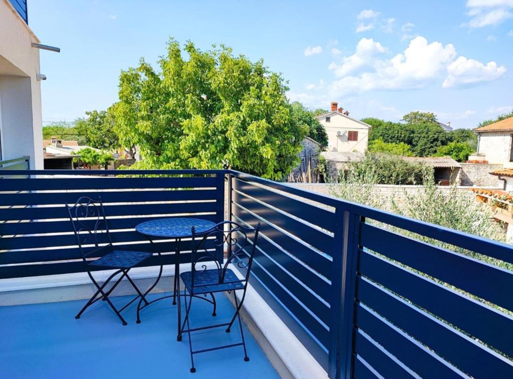 Un balcón con mesa y sillas, vista a un árbol y un edificio al fondo.