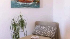 Una habitación con una cama, un almohadón, una planta y un cuadro de un velero en la pared.