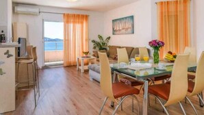 Un comedor con mesa de vidrio, cortinas naranjas y vista al mar.