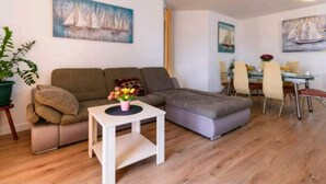 Una sala moderna con un sofá modular, una mesita blanca con un florero y un comedor con una mesa de vidrio y sillas.