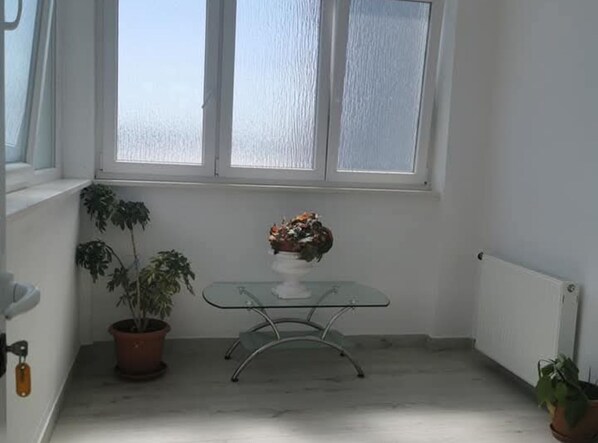 Una habitación de esquina con una planta en maceta, una mesa de vidrio con un arreglo floral y un radiador.