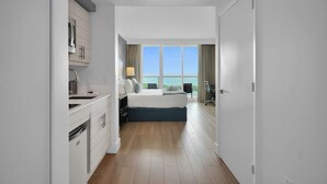 A hotel room with a bed, a desk, a chair, a window with a view of the sea, and a kitchenette. - SF Modern Comfort Steps from the Ocean Breeze (Miami)