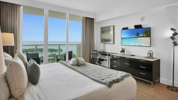A hotel room with a large bed, a desk, a TV, and a view of the ocean. - SF Modern Comfort Steps from the Ocean Breeze (Miami)