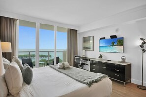 Habitación de hotel con una cama grande, un escritorio, un televisor y vista al océano.