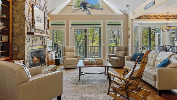 A spacious living room with a stone fireplace, comfortable seating, and a large window overlooking a deck.
