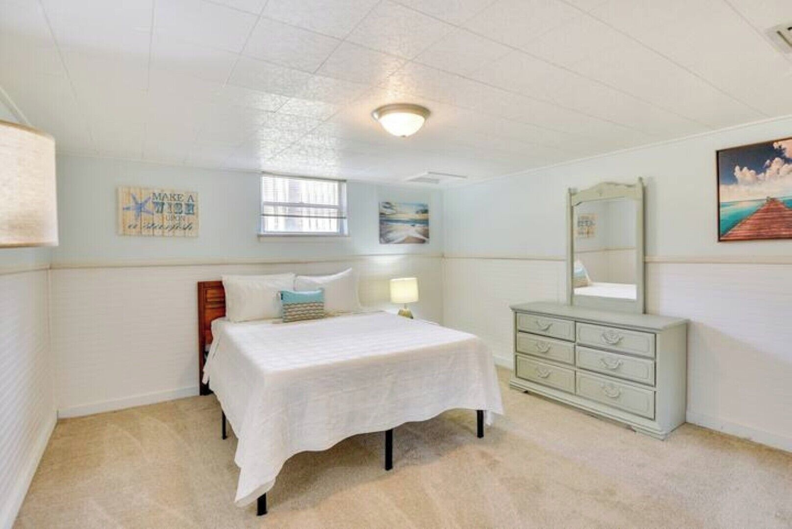 A bedroom with a bed, a dresser, a lamp, and a painting on the wall.