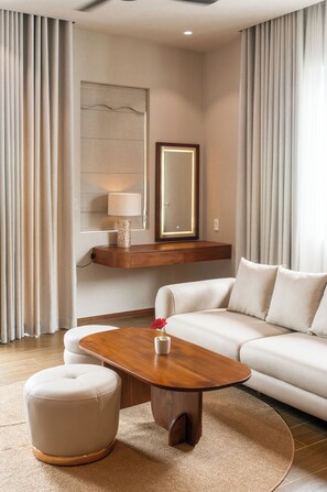 A modern hotel room with a sofa, ottoman, wooden coffee table, and a mirror.
