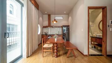 A modern kitchen with a dining area, wooden flooring, and a large window with curtains.