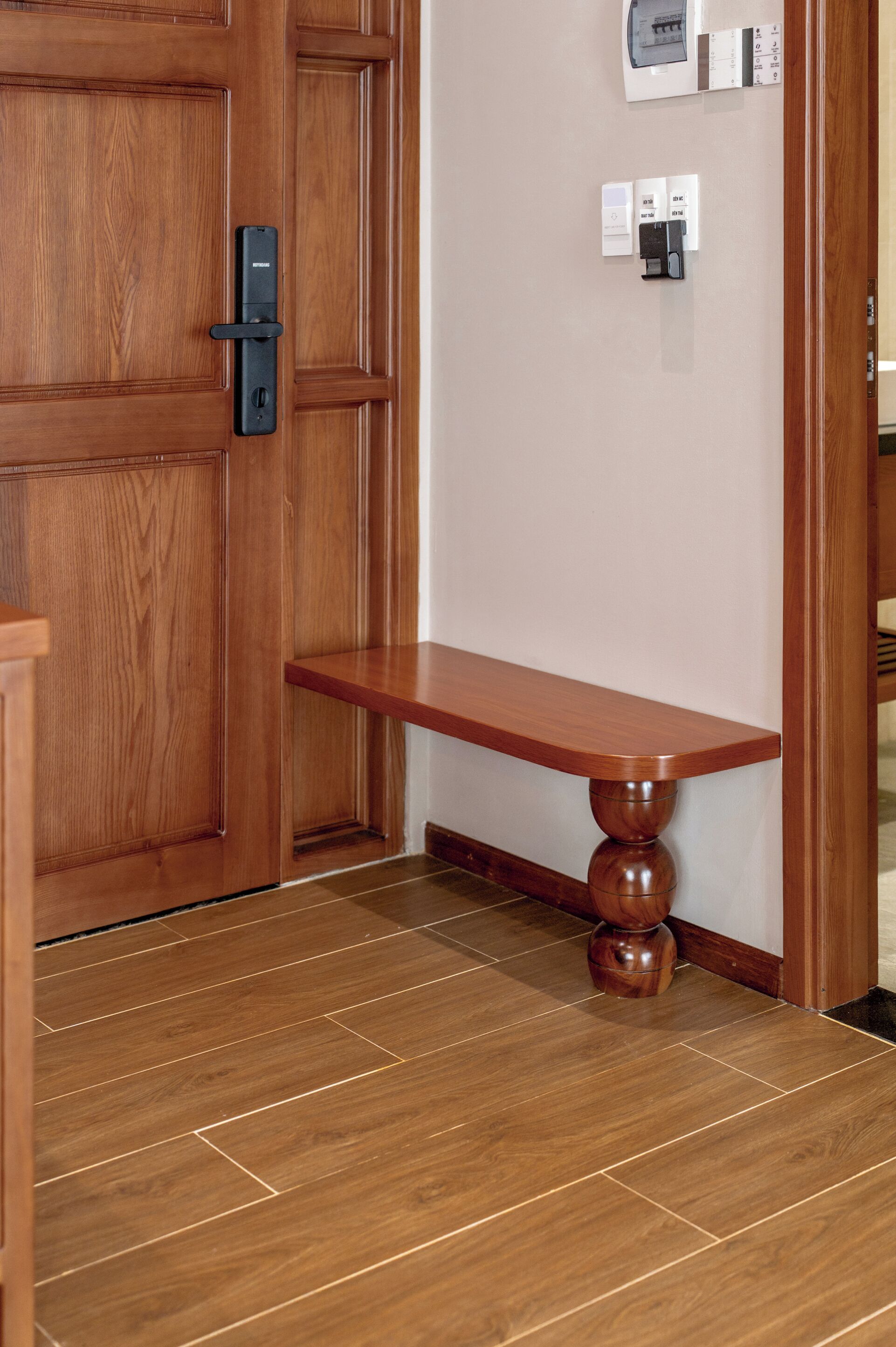 A wooden door with a keypad lock, a wooden bench, and a wall-mounted thermostat.
