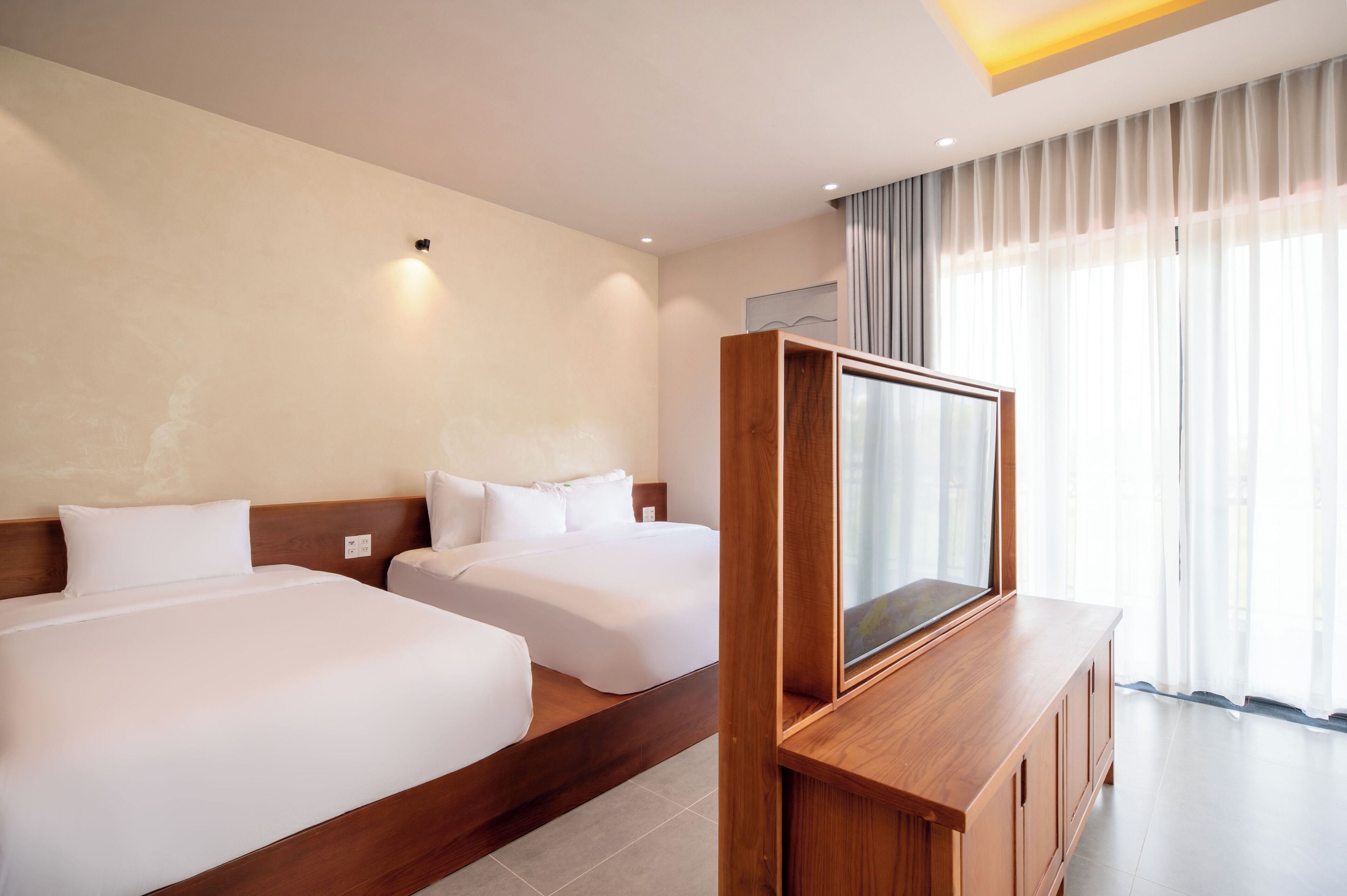 A hotel room with two beds, a wooden TV stand, and a large window with curtains.