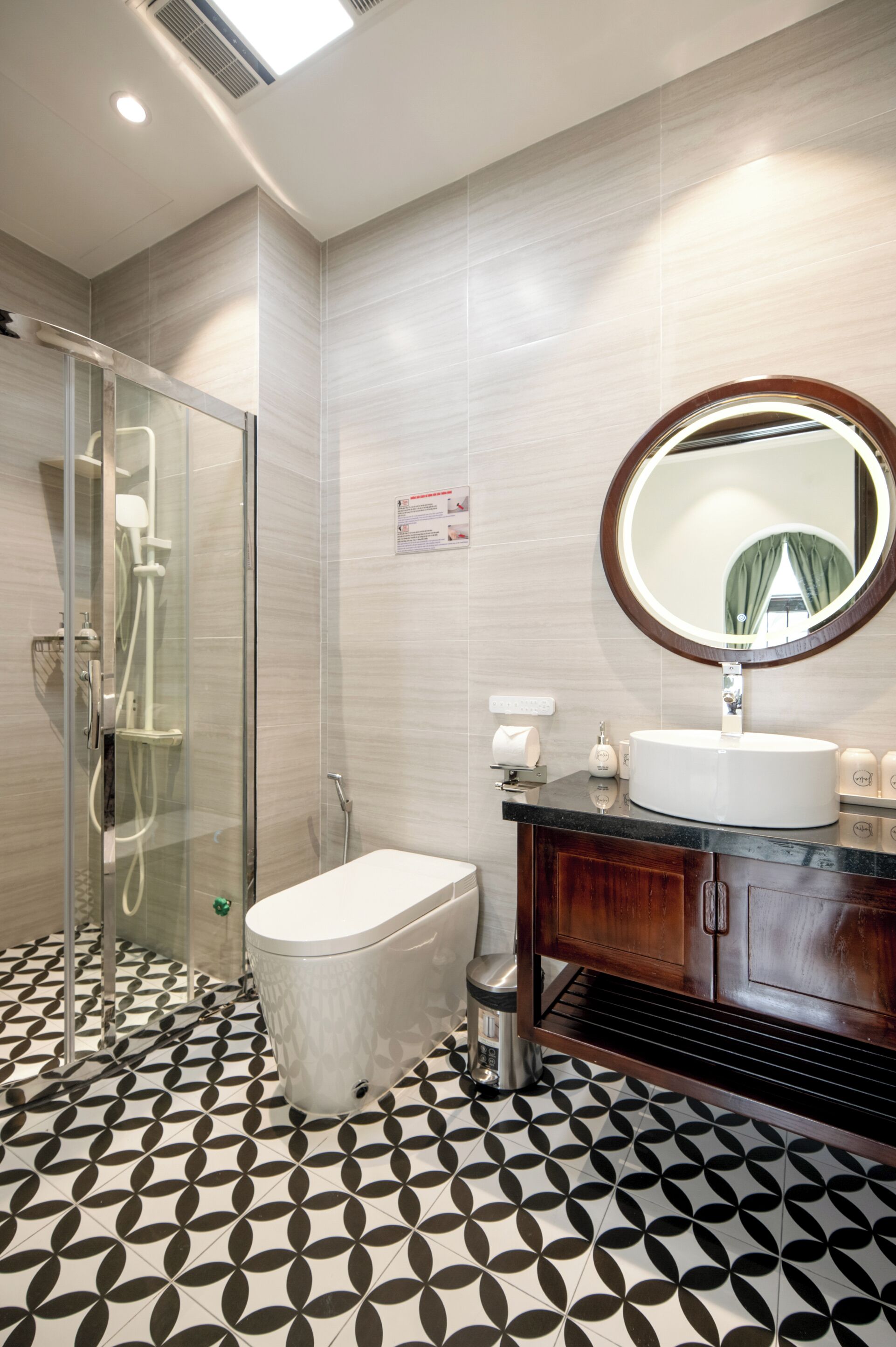 Un baño con cabina de ducha de vidrio, inodoro, lavamanos con espejo y baldosas de suelo estampadas.
