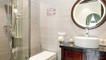 A bathroom with a glass shower enclosure, a toilet, a sink with a mirror, and patterned floor tiles.