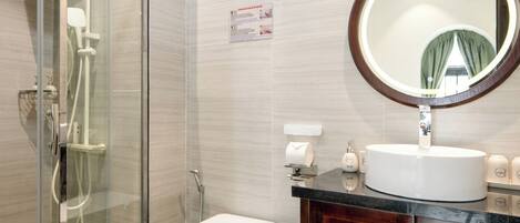 Un baño con cabina de ducha de vidrio, inodoro, lavamanos con espejo y baldosas de suelo estampadas.