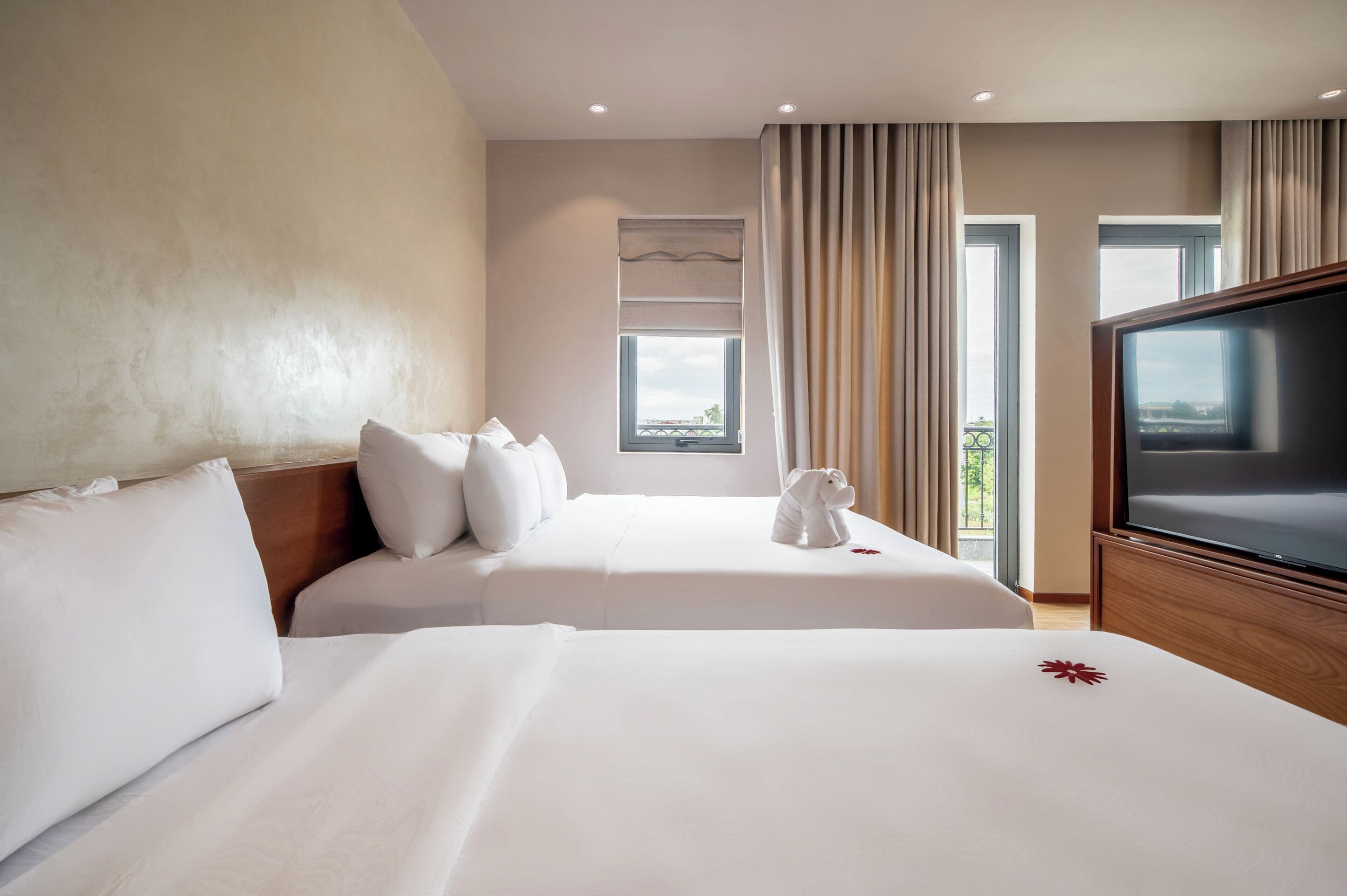 A hotel room with two beds, a television, and a view of the outdoors.