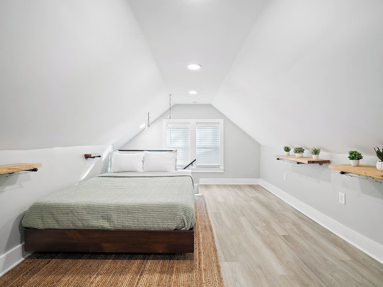 Ein Schlafzimmer mit schrägen Wänden, einem Bett, einem Fenster und Holzregalen mit Pflanzen.