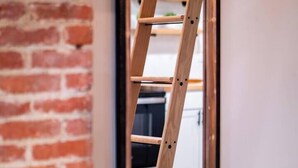 A wooden ladder leaning against a brick wall, with a white door and a glimpse of a kitchen area in the background. - Unique BOHO Ohio City Loft Apt (Cleveland)