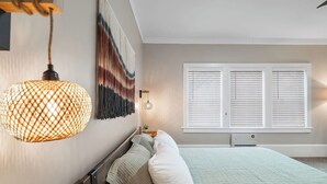 Quarto com cama, luminárias de cabeceira, tapeçaria na parede e janela com persianas.