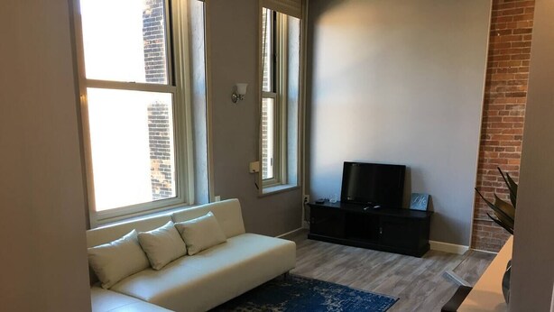 Un soggiorno moderno con un divano bianco, un tappeto blu, una TV su un supporto nero e un parete in mattoni.