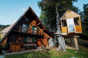 A log cabin with a treehouse attached, surrounded by a forest.