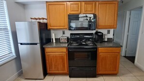 A compact kitchen with wooden cabinets, a stainless steel refrigerator, a black stove, and a microwave.