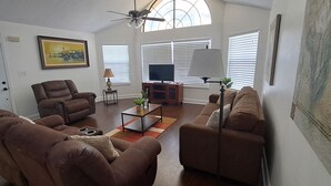 A living room with brown sofas, a coffee table, a TV, and a ceiling fan.
