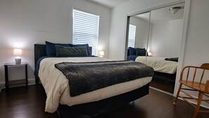 A bedroom with a bed, bedside tables, a chair, a mirror, and a window with blinds.