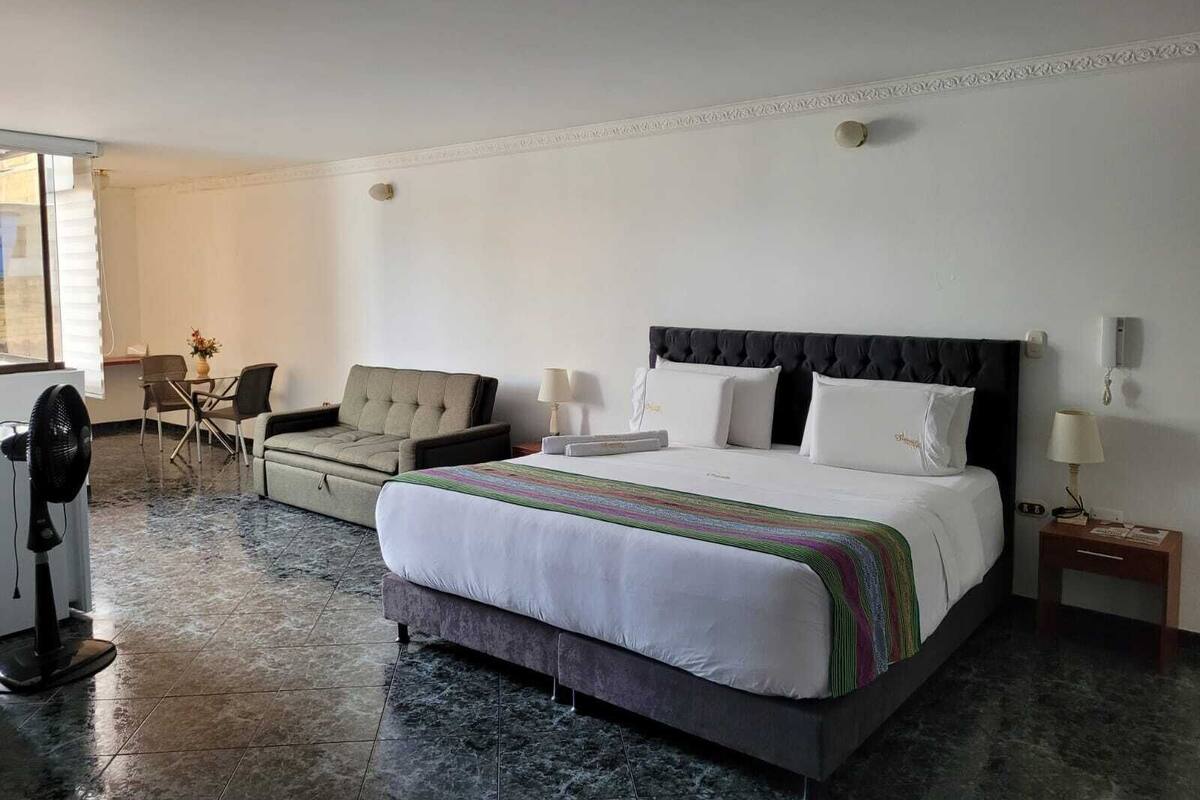 Une chambre d’hôtel avec un lit, un canapé, un bureau et un ventilateur.