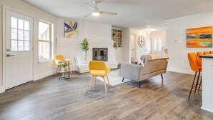 A spacious living room with hardwood flooring, a fireplace, a ceiling fan, and a dining area with bar stools. - The Eclectic Oasis - Pool, Games & Family Fun (Grand Prairie)