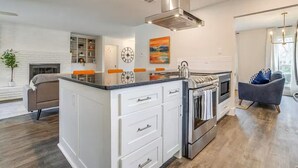 A modern kitchen with a central island, built-in oven, and stainless steel range hood. - The Eclectic Oasis - Pool, Games & Family Fun (Grand Prairie)