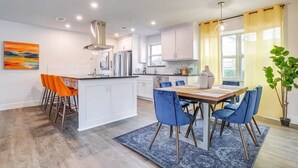 A modern kitchen with white cabinets, a central island, and blue chairs. - The Eclectic Oasis - Pool, Games & Family Fun (Grand Prairie)