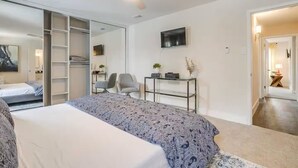 A modern bedroom with a large bed, a desk, a chair, a TV, and a sliding closet door. - The Eclectic Oasis - Pool, Games & Family Fun (Grand Prairie)
