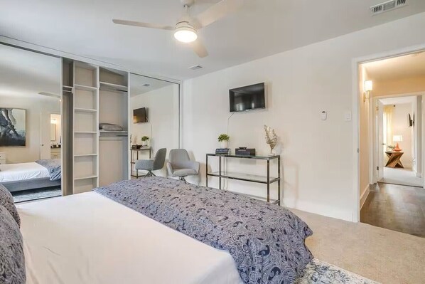 A modern bedroom with a large bed, a desk, a chair, a TV, and a sliding closet door.