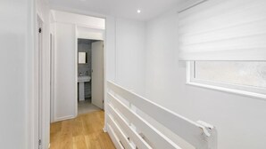 Un pasillo estrecho con suelo de madera, paredes blancas y una ventana con persianas.