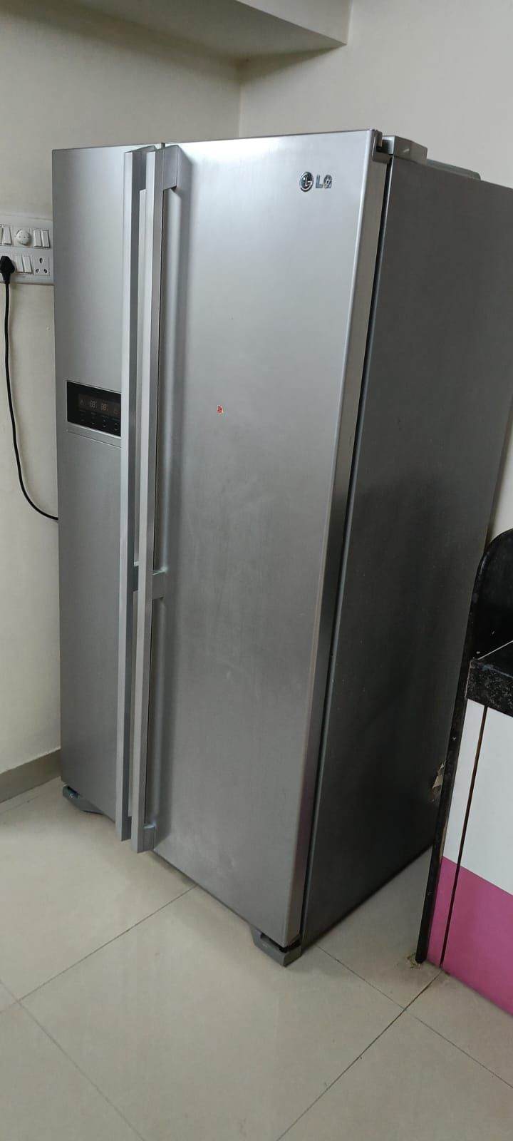 A stainless steel LG refrigerator in a kitchen with a tiled floor and a pink wall.