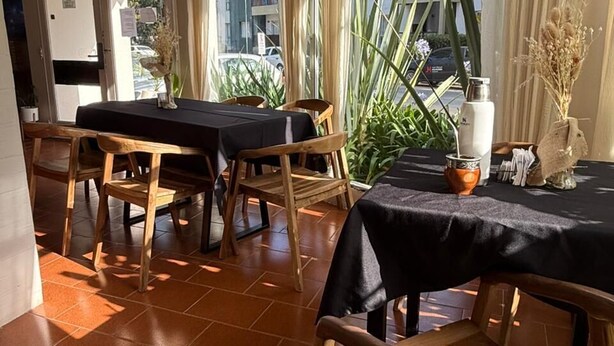 A dining area with wooden chairs and tables, large windows with curtains, and a view of buildings outside. - Black Suites Pinamar  (Pinamar)