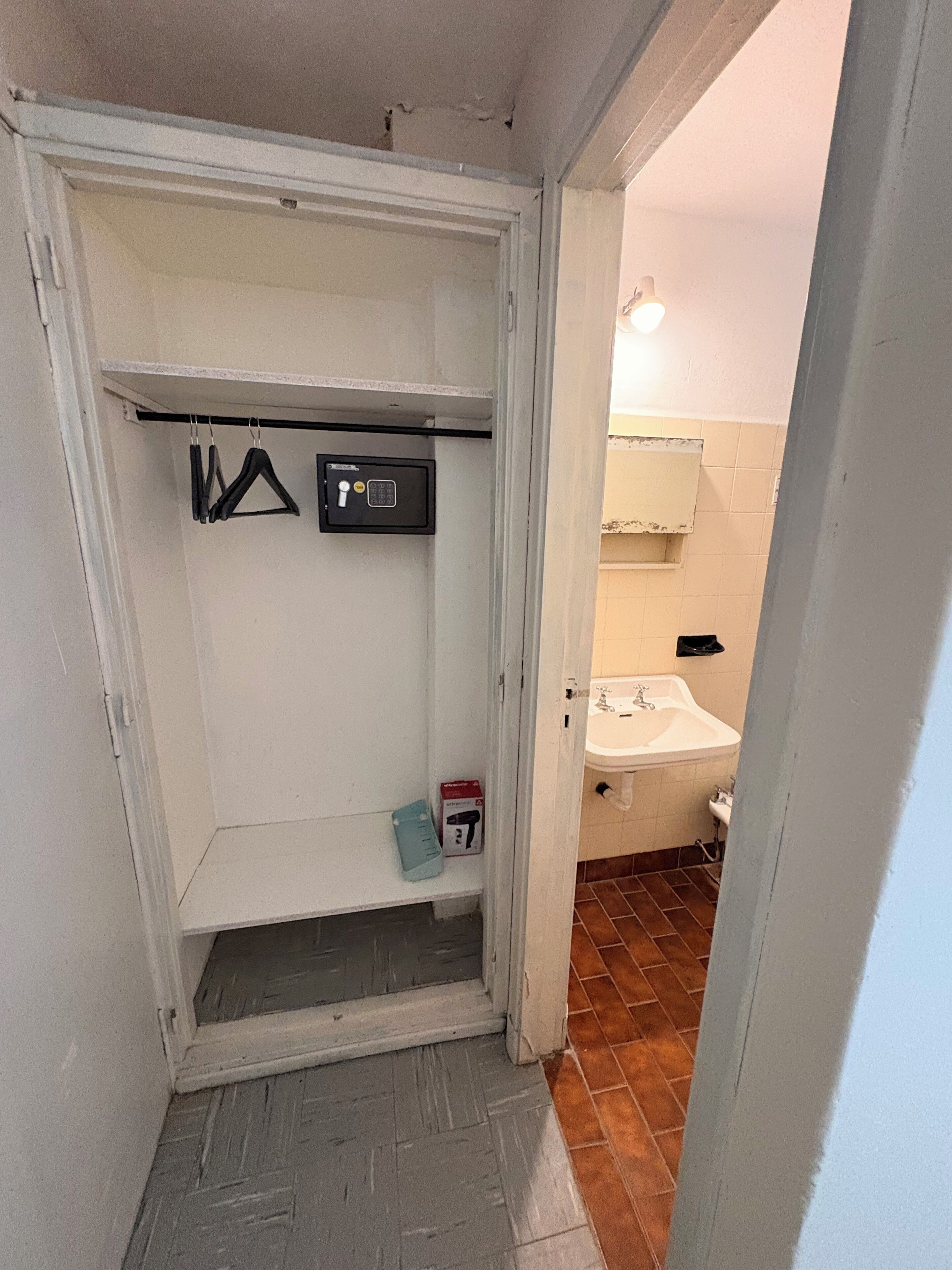 Een compacte, afgesloten badkamer met een witte wastafel, een spiegel en een handdoekhouder.