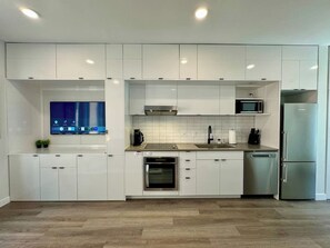 A modern kitchen with white cabinets, a built-in oven, a microwave, and a stainless steel refrigerator.