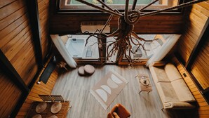 A high-ceilinged room with a wooden floor, a hanging rope chandelier, a sofa, a coffee table, and a view of a hot tub through a window. - Sapanca Özfer Bungalov (Sapanca)