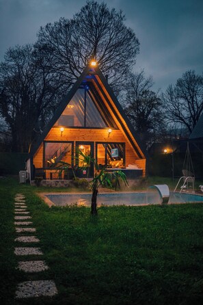 Een modern huis met een glazen voorgevel, een zwembad en een houten terras.
