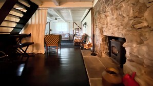 Un salón acogedor con chimenea de piedra, un sillón a cuadros y una escalera de madera.