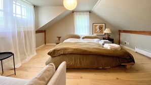 Un dormitorio con una cama grande, una mesita de noche, una lámpara y una ventana con cortinas translúcidas.