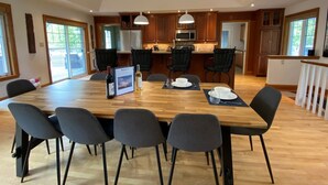 A spacious dining area with a large wooden table, black chairs, and pendant lighting. - Private Beach, Hot Tub, A Vacay to Remember! (Prince Edward)