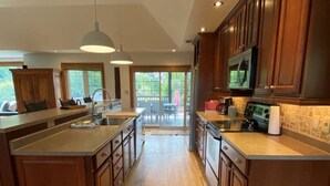 A spacious kitchen with wooden cabinets, a central island, and a view to an outdoor patio. - Private Beach, Hot Tub, A Vacay to Remember! (Prince Edward)