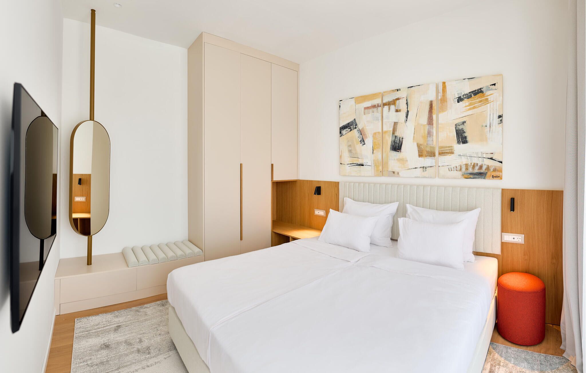 A modern hotel room with a large bed, a flat-screen TV, a wooden headboard, and abstract art on the wall.