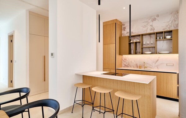 A modern kitchen with a central island, bar stools, wooden cabinets, and a backsplash with a floral pattern.