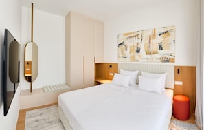 A modern hotel room with a large bed, a flat-screen TV, a wooden headboard, and abstract art on the wall.