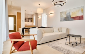 Uma sala de estar moderna com um sofá, uma poltrona vermelha, uma mesa de jantar e um criado-mudo preto.